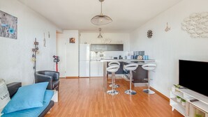Un salon moderne avec un canapé, un téléviseur et un coin cuisine équipé de tabourets de bar.