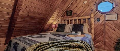Un dormitorio de buhardilla acogedor, con techo inclinado de madera, una cama con colcha y un ventanal pequeño.