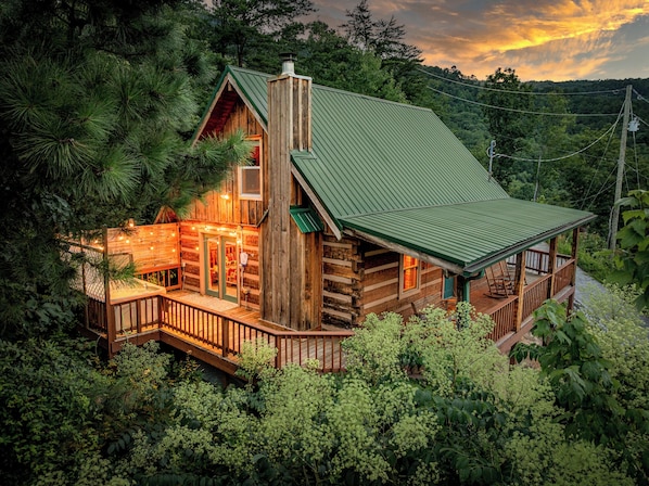 A log cabin with a green metal roof, a porch, and a chimney.