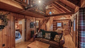 Een gezellig blokhutinterieur met een leren bank, houten tafels en een trap naar een hoger niveau.
