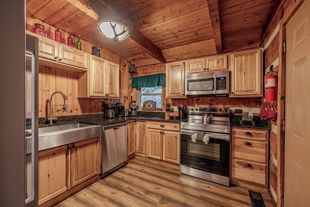 Una cocina de estilo cabaña de madera con un refrigerador, microondas, horno y lavavajillas de acero inoxidable.