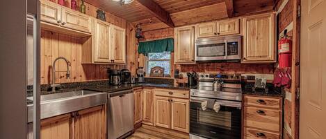 Una cocina de estilo cabaña de madera con un refrigerador, microondas, horno y lavavajillas de acero inoxidable.