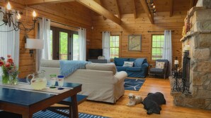 A cozy cabin interior with wooden walls, a stone fireplace, a sofa, a television, and a dog lying on the floor. - Wiggleswick Cottage; Dogs Welcome Certified! 9/17-9/19 available! (Georgetown)