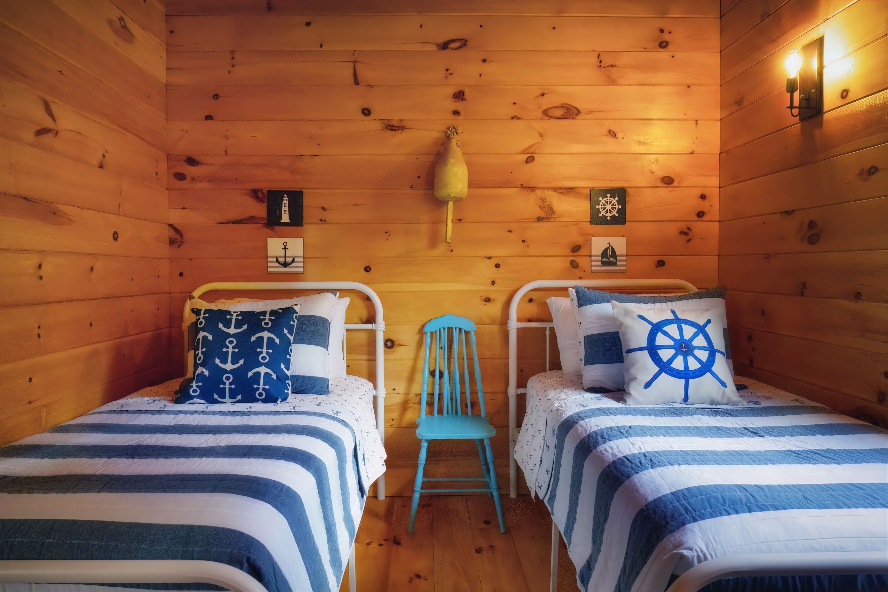 A cabin with two beds, each with a striped blue and white bedding, a blue chair, and nautical-themed wall decor.