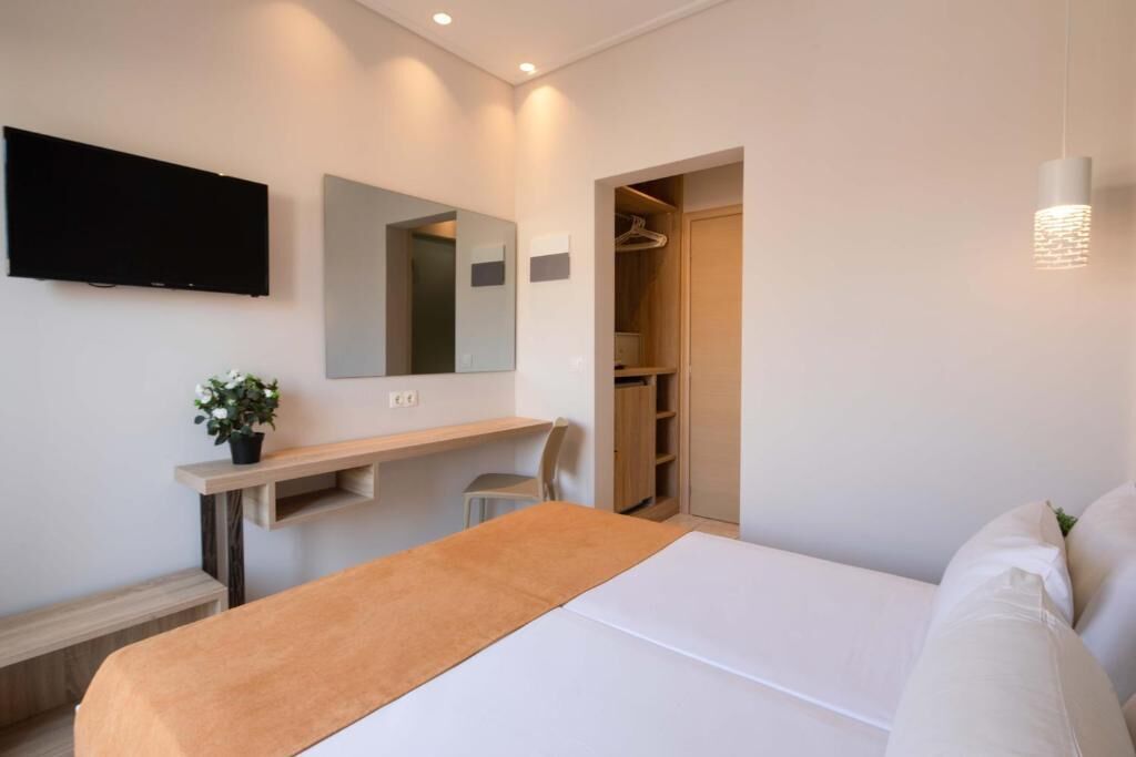 A hotel room with a bed, a TV mounted on the wall, a mirror, a bedside table, and a wardrobe.