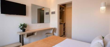 A hotel room with a bed, a TV mounted on the wall, a mirror, a bedside table, and a wardrobe.