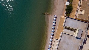 Vista aérea de un hotel costero con ubicación frente a la playa, una fila de sombrillas y un edificio de techo plano.