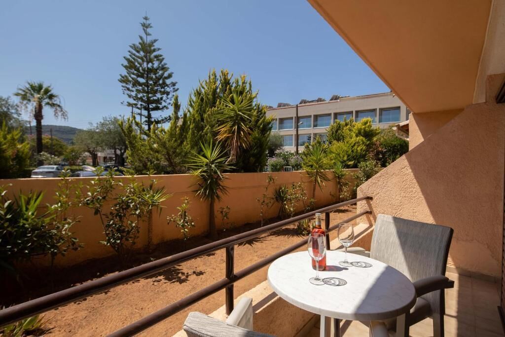 A balcony with a table and chairs, a bottle of wine, and a view of a building and trees.