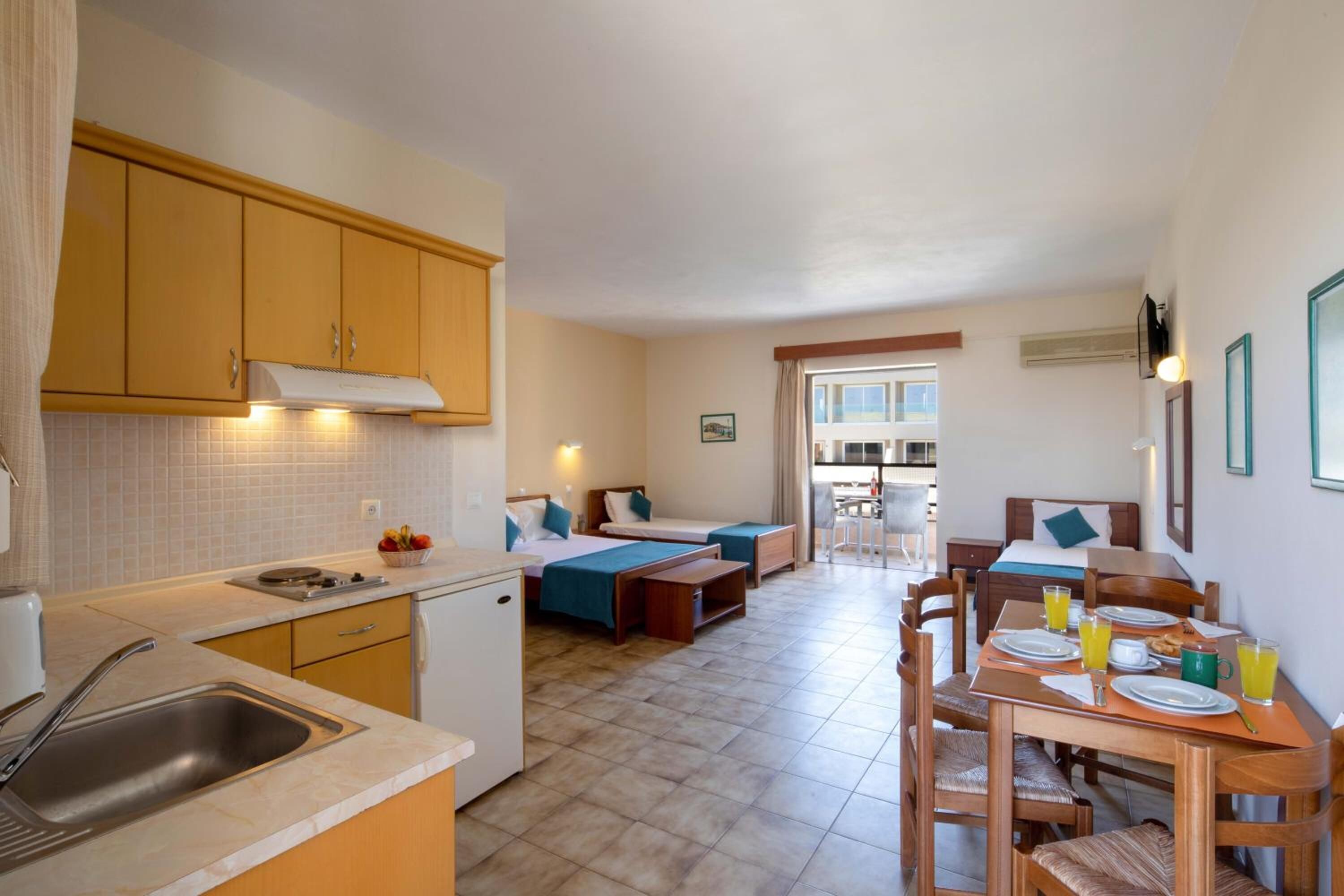 Een compacte hotelkamer met een kitchenette, twee eenpersoonsbedden, een eethoek en een badkamer.