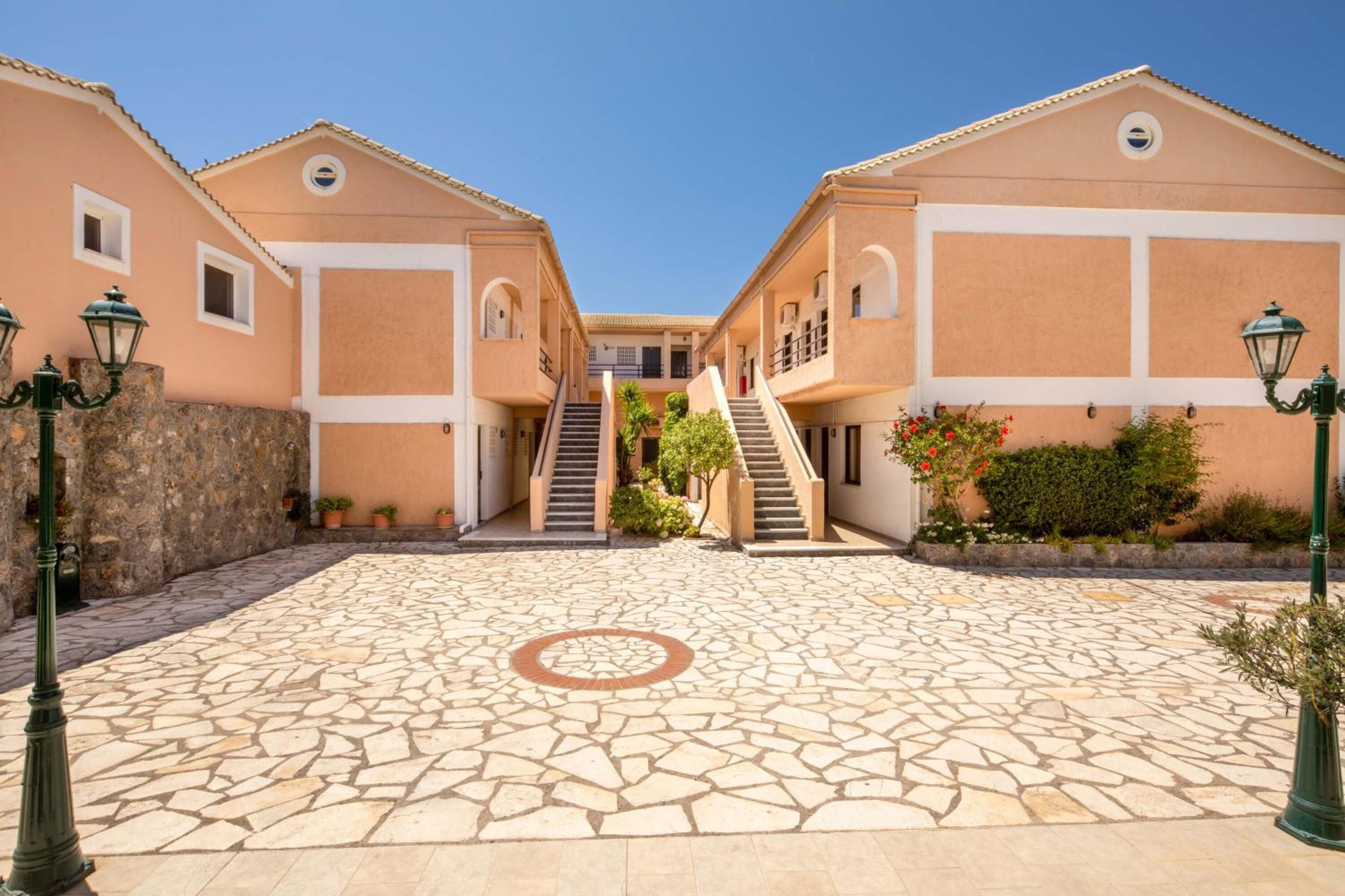 A courtyard with a stone floor, two-story buildings with balconies, and a central staircase.