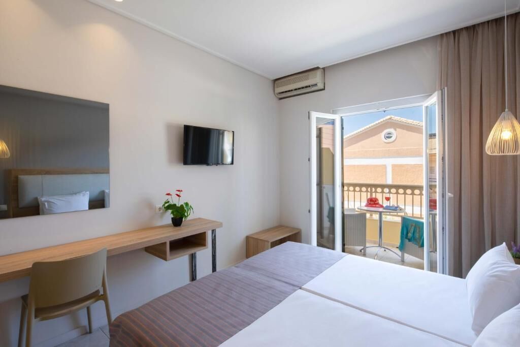 Ein Hotelzimmer mit einem Bett, einem Schreibtisch, einem Sessel, einem Fernseher und einem Balkon mit Tisch und Stühlen.