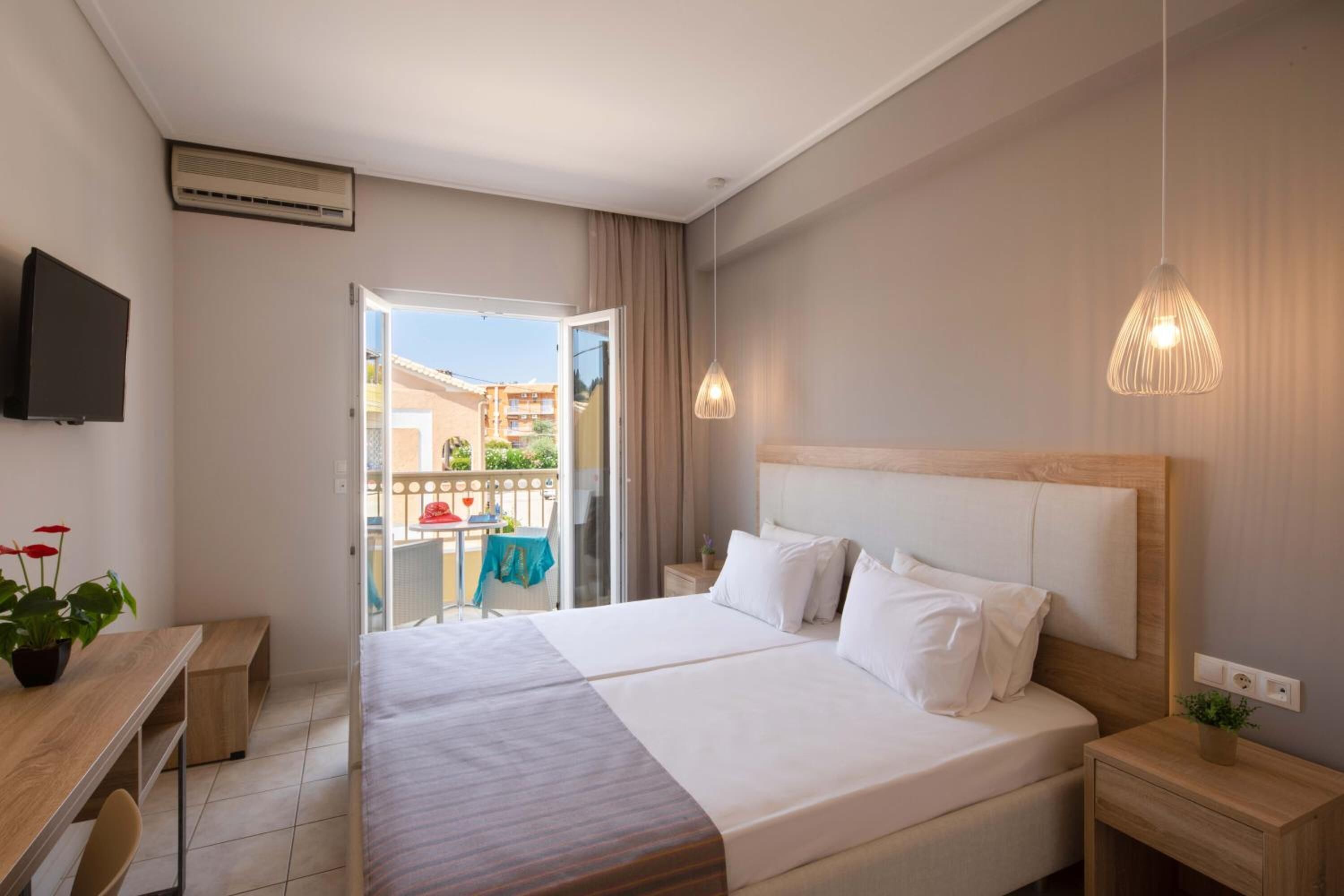 A hotel room with a large bed, a desk, a television, and a balcony with a table and chairs.
