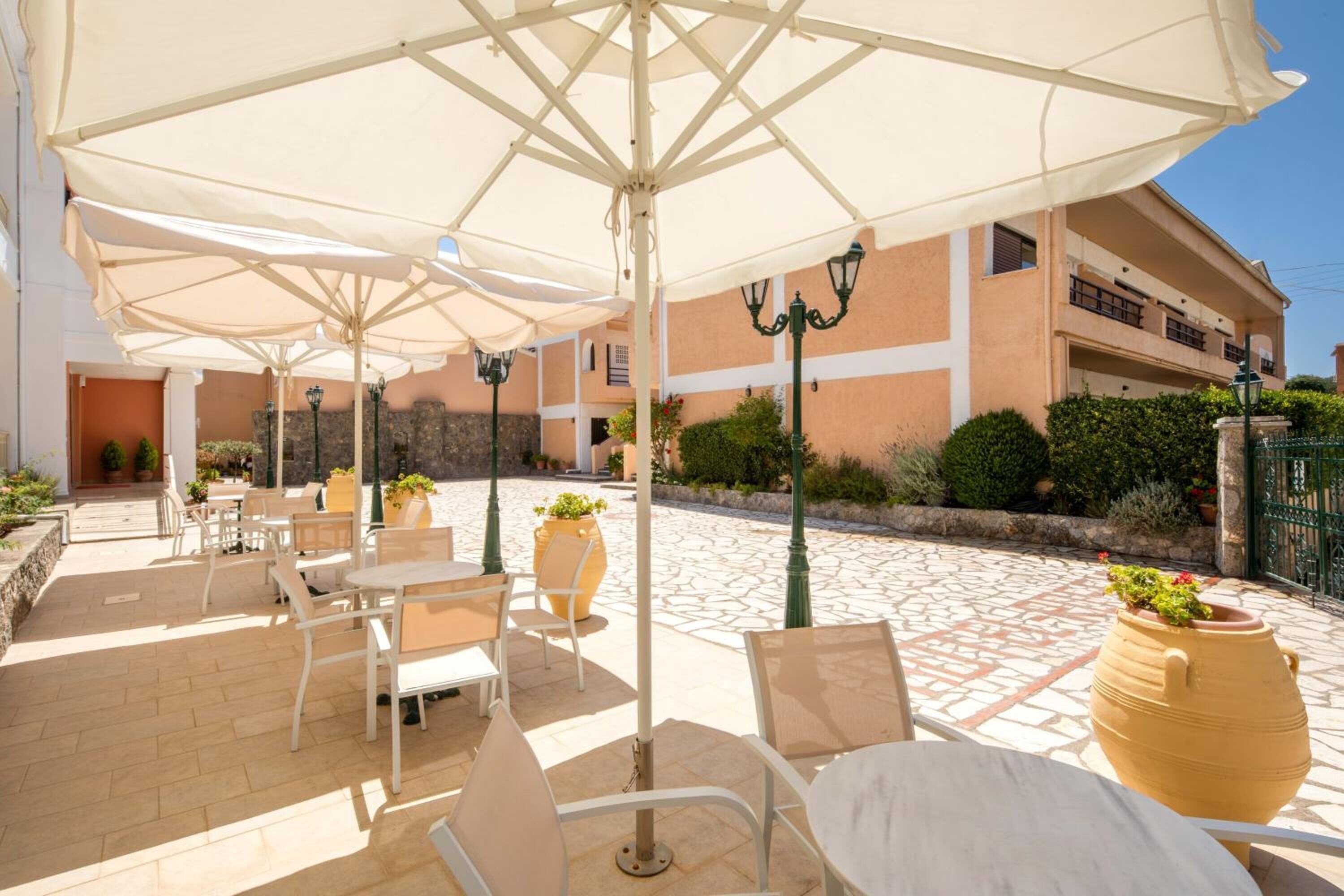 An outdoor patio with white tables and chairs, large umbrellas, and potted plants.