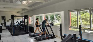 Academia com esteiras, máquinas de peso e uma grande janela que oferece luz natural.