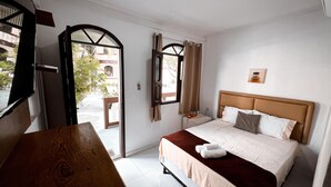 Une chambre d’hôtel avec un lit, un banc en bois, une fenêtre avec des rideaux et une vue sur l’extérieur.
