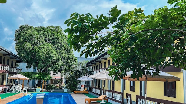 Un espace piscine doté de chaises longues et de parasols, entouré d’immeubles avec balcons.