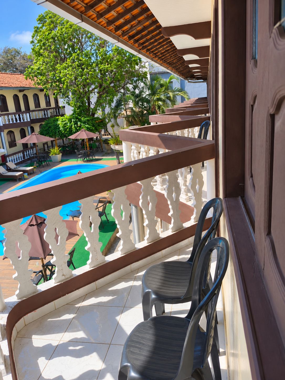 A balcony with a view of a swimming pool, outdoor furniture, and a building with arches.