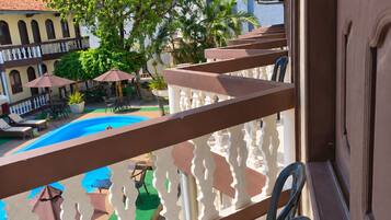 A balcony with a view of a swimming pool, outdoor furniture, and a building with arches.