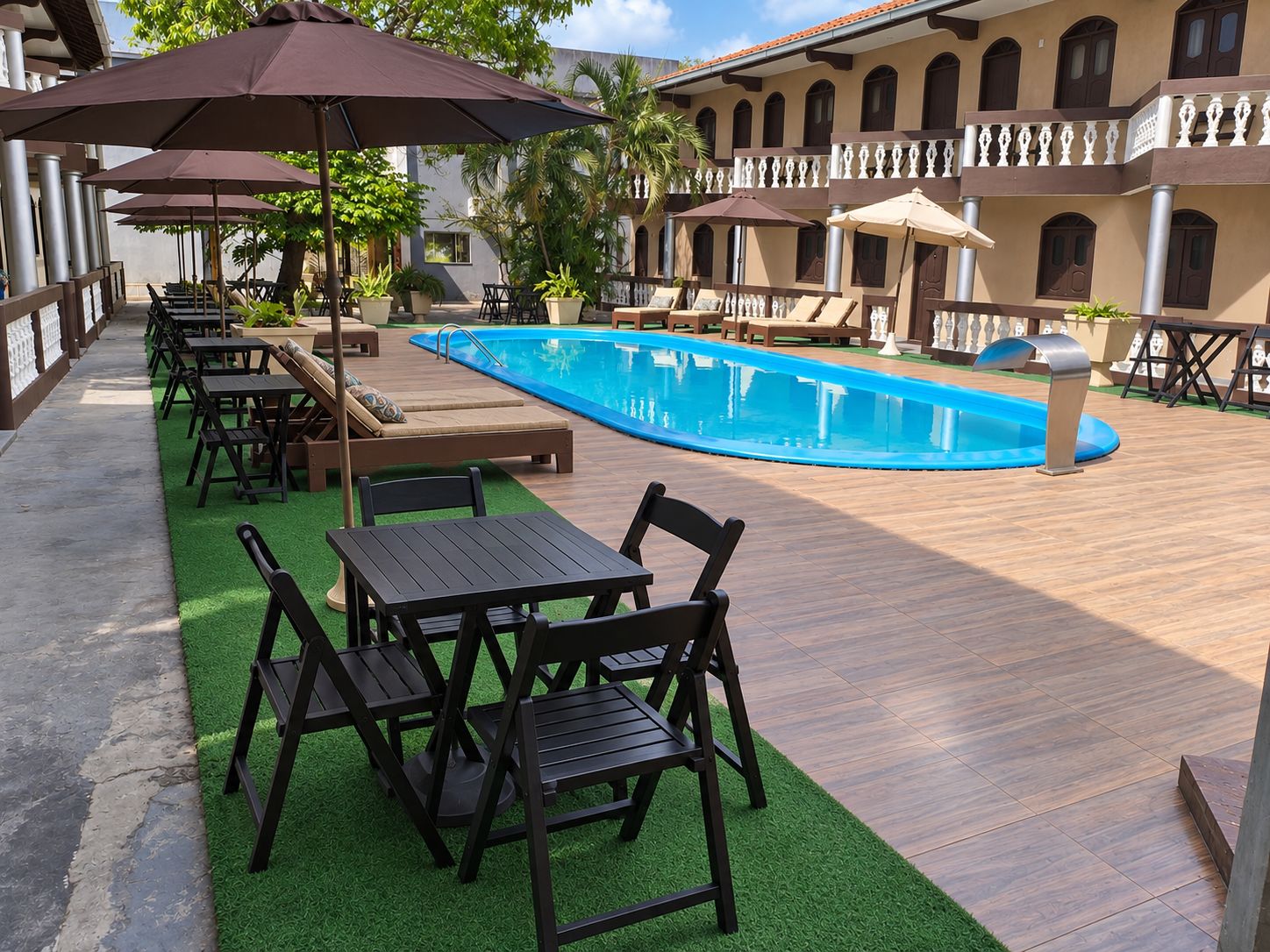 A poolside area with lounge chairs and tables, a swimming pool, and a building with balconies.