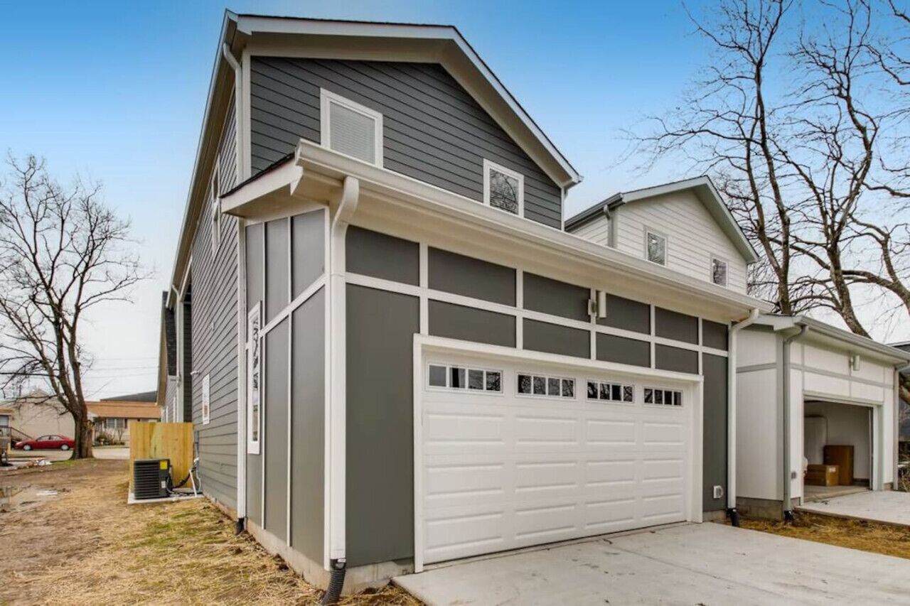 Une maison à deux étages avec un garage, une allée couverte et une petite cour avec des arbres sans feuilles.