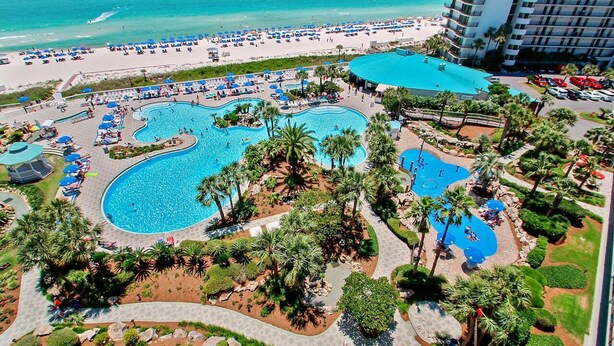 Ein Resort mit mehreren Schwimmbecken, einem Strand und einem hohen Hotelgebäude.