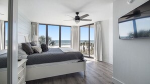 Ein Schlafzimmer mit Bett, Deckenventilator, Fernseher und Blick auf den Ozean.