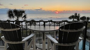 Eine Terrasse mit zwei Adirondack-Stühlen, die auf einen Sonnenuntergang über dem Meer blicken.