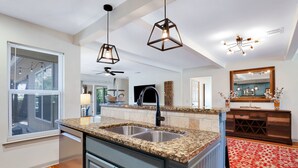 Une cuisine moderne dotée de plans de travail en granit, d’appareils électroménagers en acier inoxydable et de luminaires suspendus.