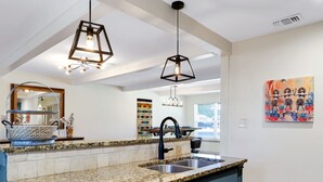 Une cuisine moderne dotée de plans de travail en granit, d’appareils électroménagers en acier inoxydable et de luminaires suspendus.