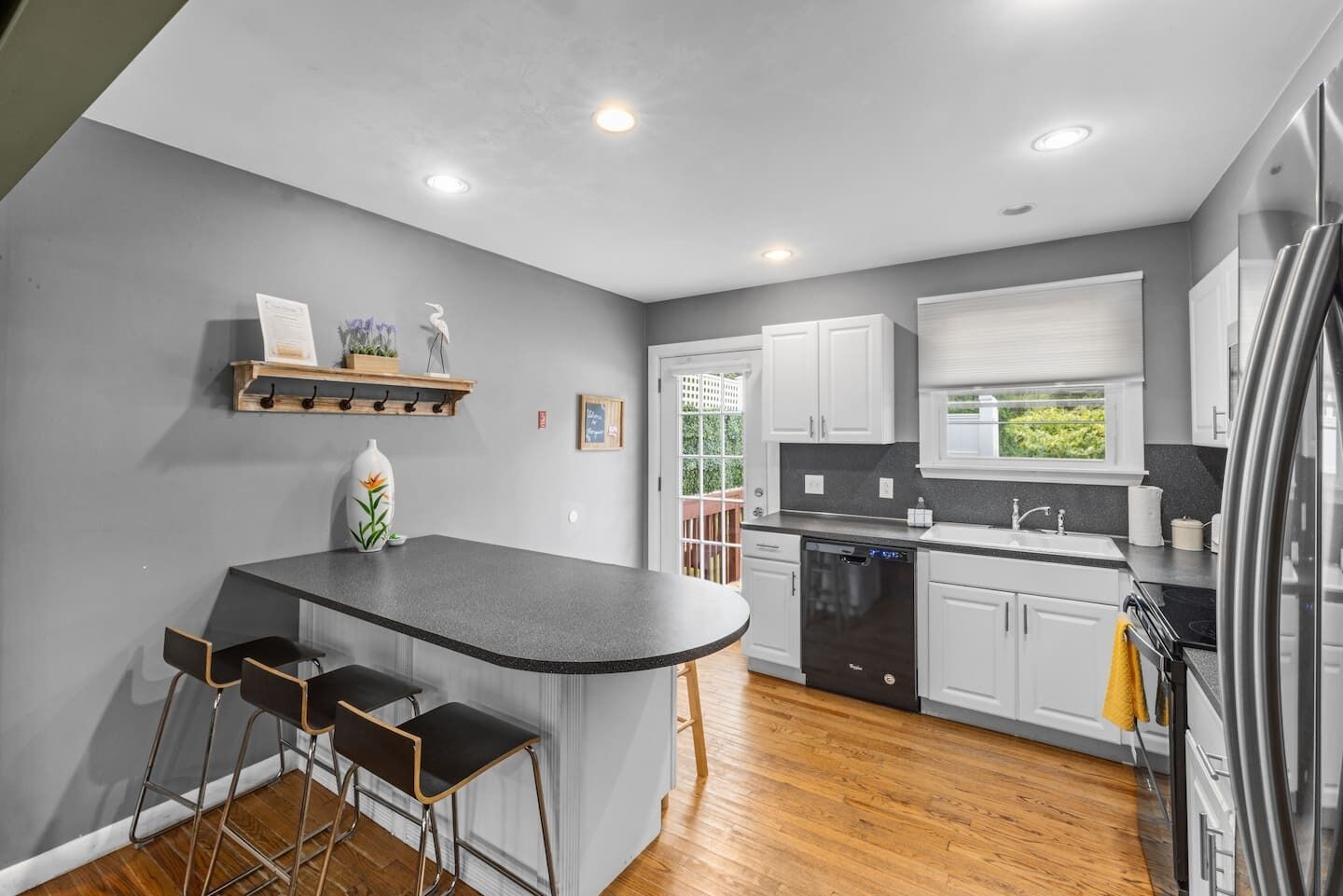 Una cocina moderna con una isla central, taburetes de bar, armarios blancos, lavavajillas y un refrigerador.