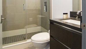 A modern bathroom with a glass-enclosed shower, a white toilet, and a dark wooden vanity with a mirror.
