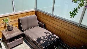 A sunlit corner with a cushioned bench, a wicker table, and a potted plant.