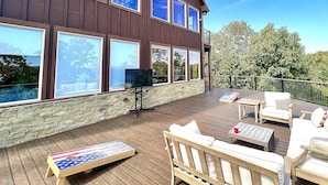 A wooden deck with outdoor furniture, a stone wall, and large windows.