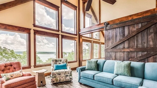 A spacious room with large windows, a blue sofa, a red armchair, and a patterned ottoman.