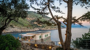 A coastal building with a stone pathway, a view of the sea, and a mountainous backdrop. - Isca Private Island (Massa Lubrense)