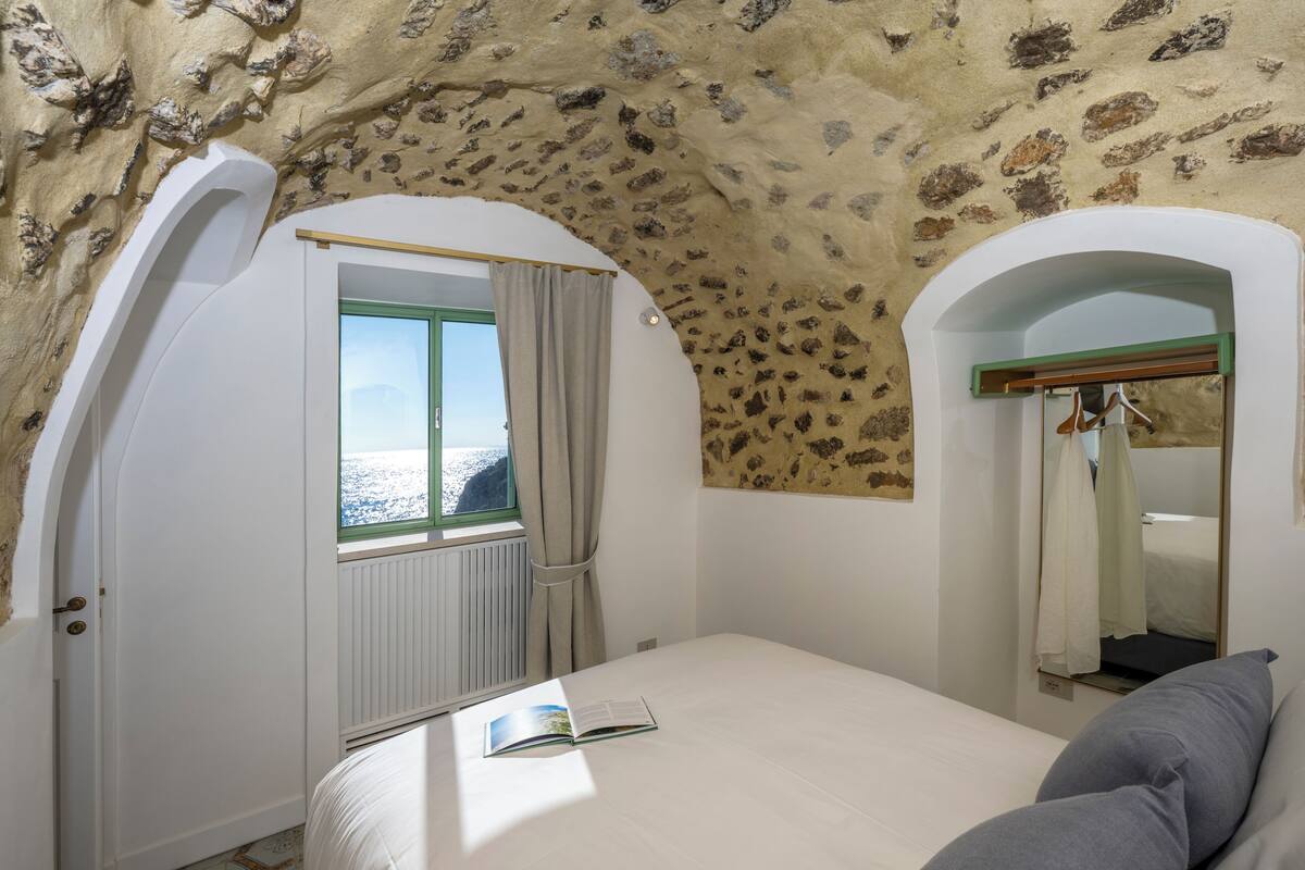 A bedroom with a sloped ceiling, a window with curtains, a bed, and a mirror.