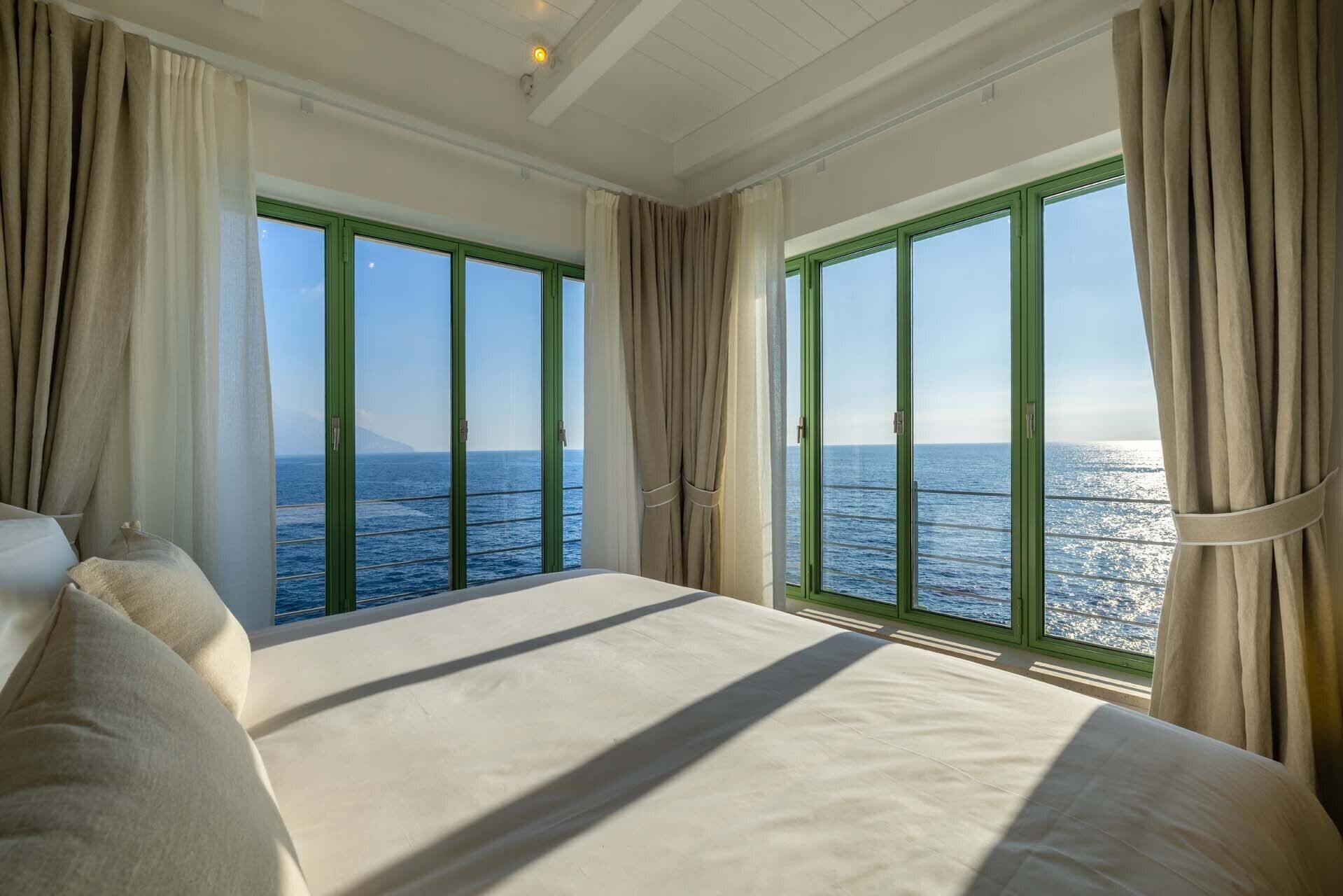 Ein Schlafzimmer mit einem großen Bett, zwei Vorhängen und Meerblick.