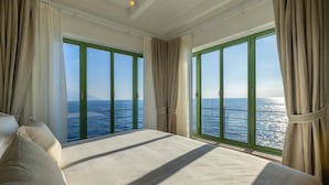 Un dormitorio con una cama grande, dos ventanas con cortinas y vista al mar.