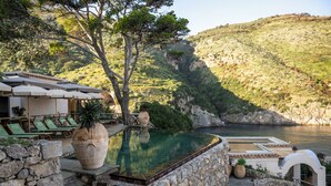 Une piscine avec des marches en pierre, des chaises longues et une vue sur un paysage montagneux.