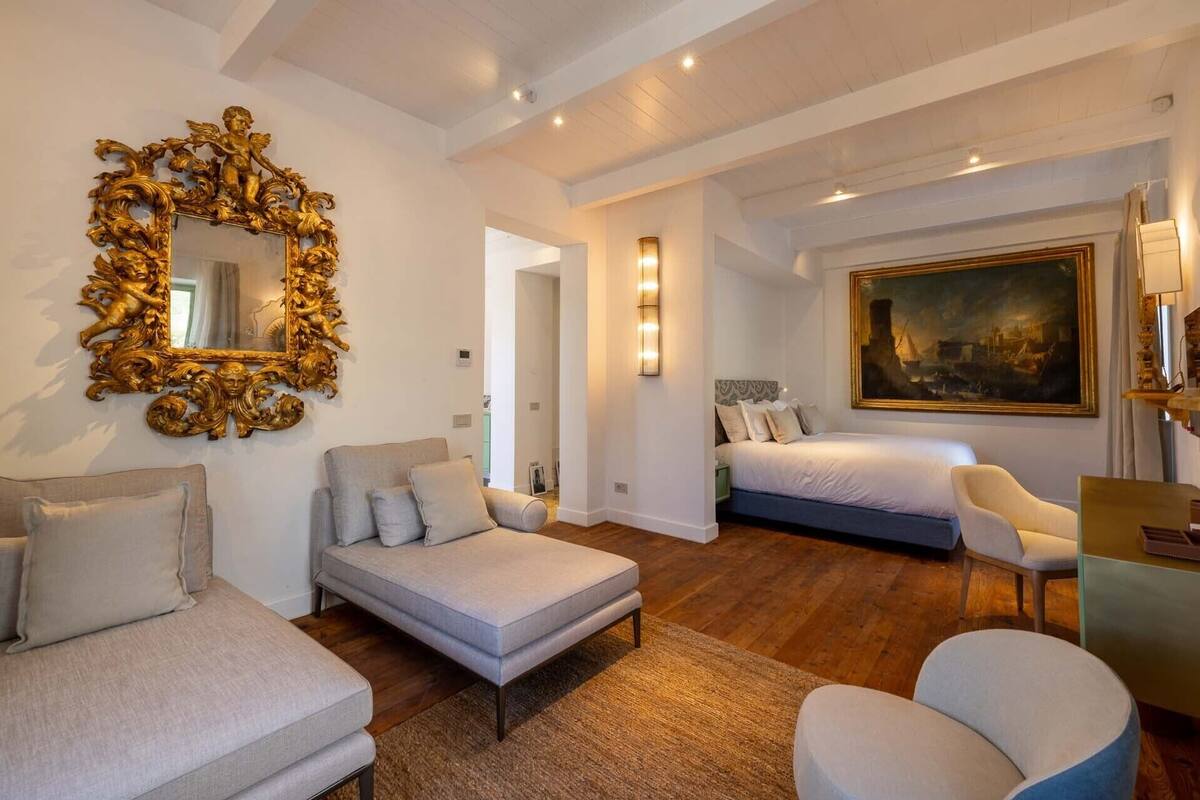 A spacious bedroom with a large bed, a sofa, a chair, and a decorative mirror.