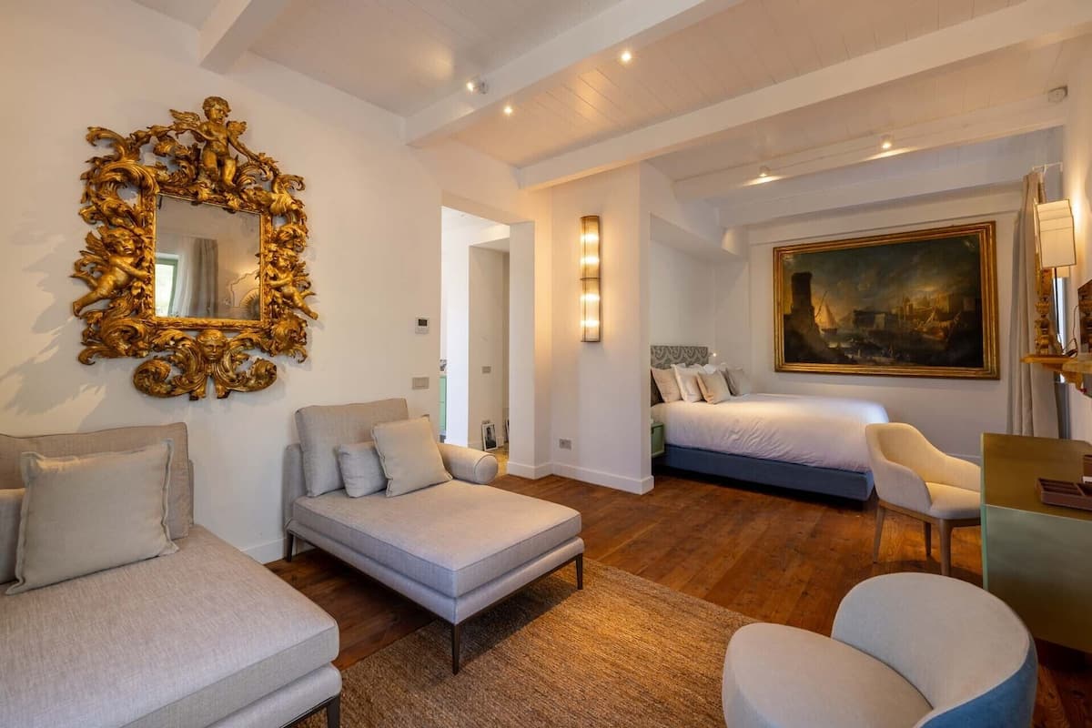 A spacious bedroom with a large bed, a sofa, a chair, and a decorative mirror.