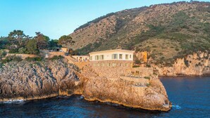 Una propiedad costera con un edificio de piedra, piscina y vistas al mar y las colinas.