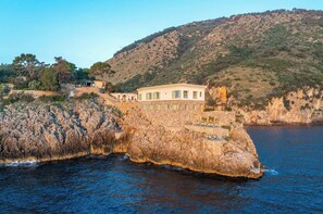 A coastal property with a stone building, a pool, and a view of the sea and hills.