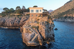Una casa de piedra con balcón sobre un acantilado rocoso con vista al agua.