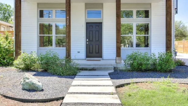 Une maison de plain-pied avec un porche à l’avant, une porte d’entrée sombre et le numéro « 422 » peint sur le mur.