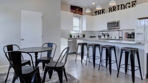 Une cuisine moderne avec des meubles blancs, un îlot central doté de tabourets de bar, des luminaires suspendus et un four à micro-ondes.