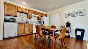 Une cuisine compacte avec des meubles de rangement en bois, une table à manger avec des chaises, une horloge et une poubelle.