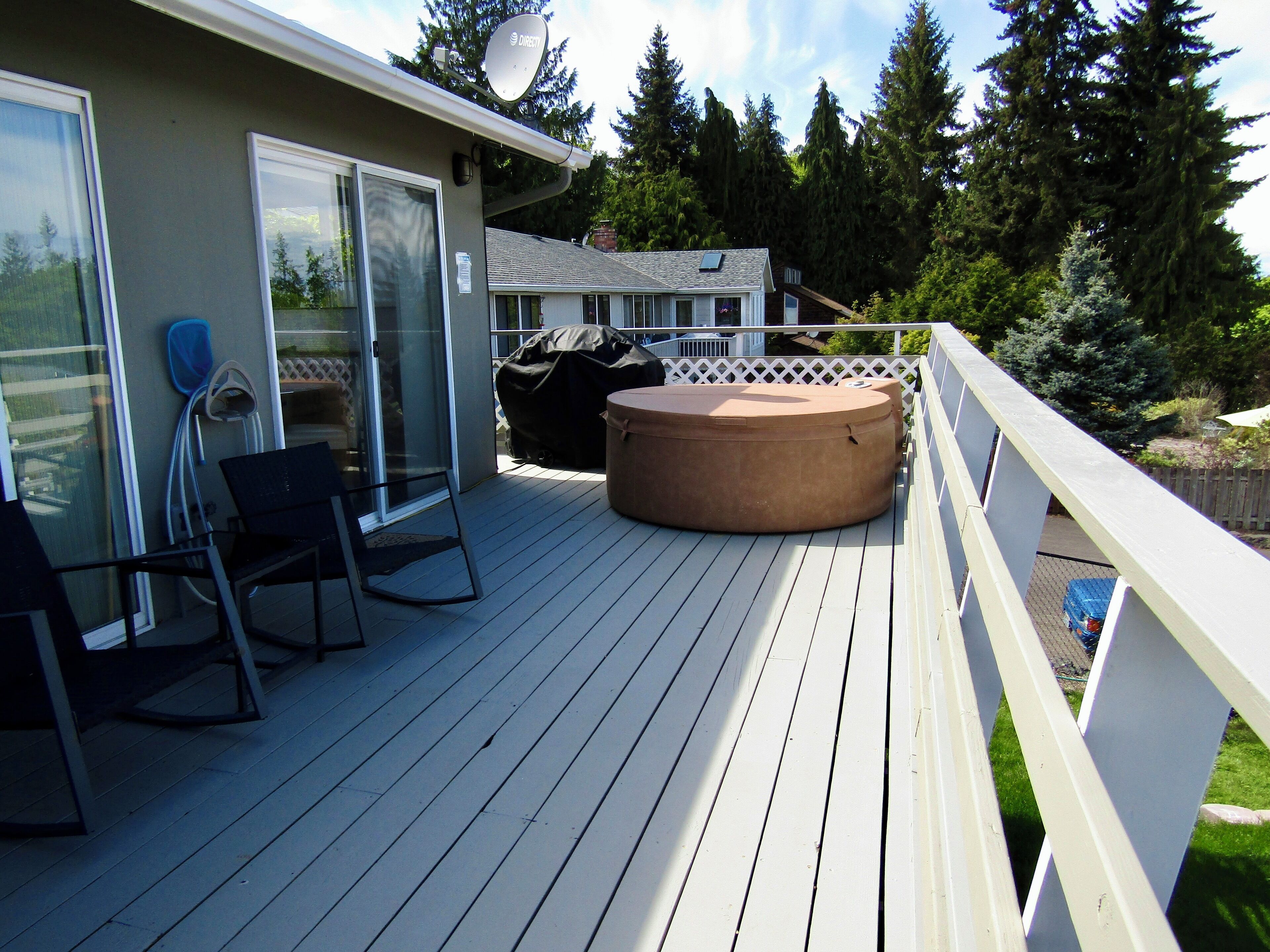 Une terrasse avec un jacuzzi, des chaises et un barbecue couvert.