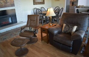 A living room with a fireplace, leather sofa, armchair, and dining table with chairs.