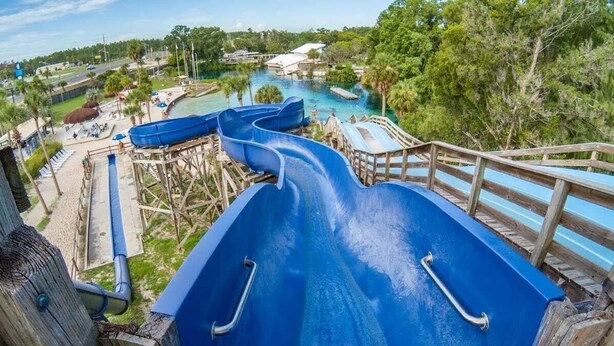 A water park with multiple blue slides and a wooden deck overlooking a pool area. - "Shore Fun, Bare Feet Retreat" (Spring Hill)